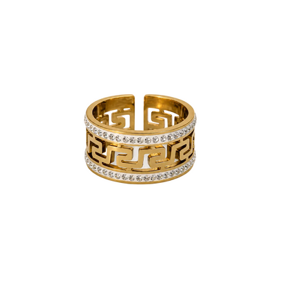 A gold ring with a Greek key pattern and clear stones, displayed on a white background with small white flowers in the corners.