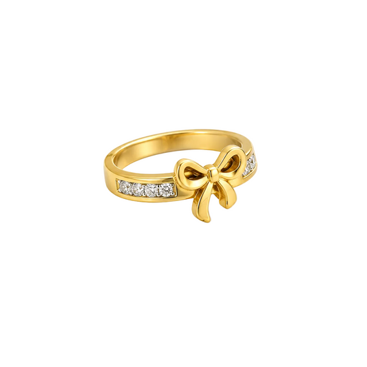 A gold ring featuring a bow-shaped centerpiece and rows of small clear stones on the band, styled with white baby's breath flowers on a white background.